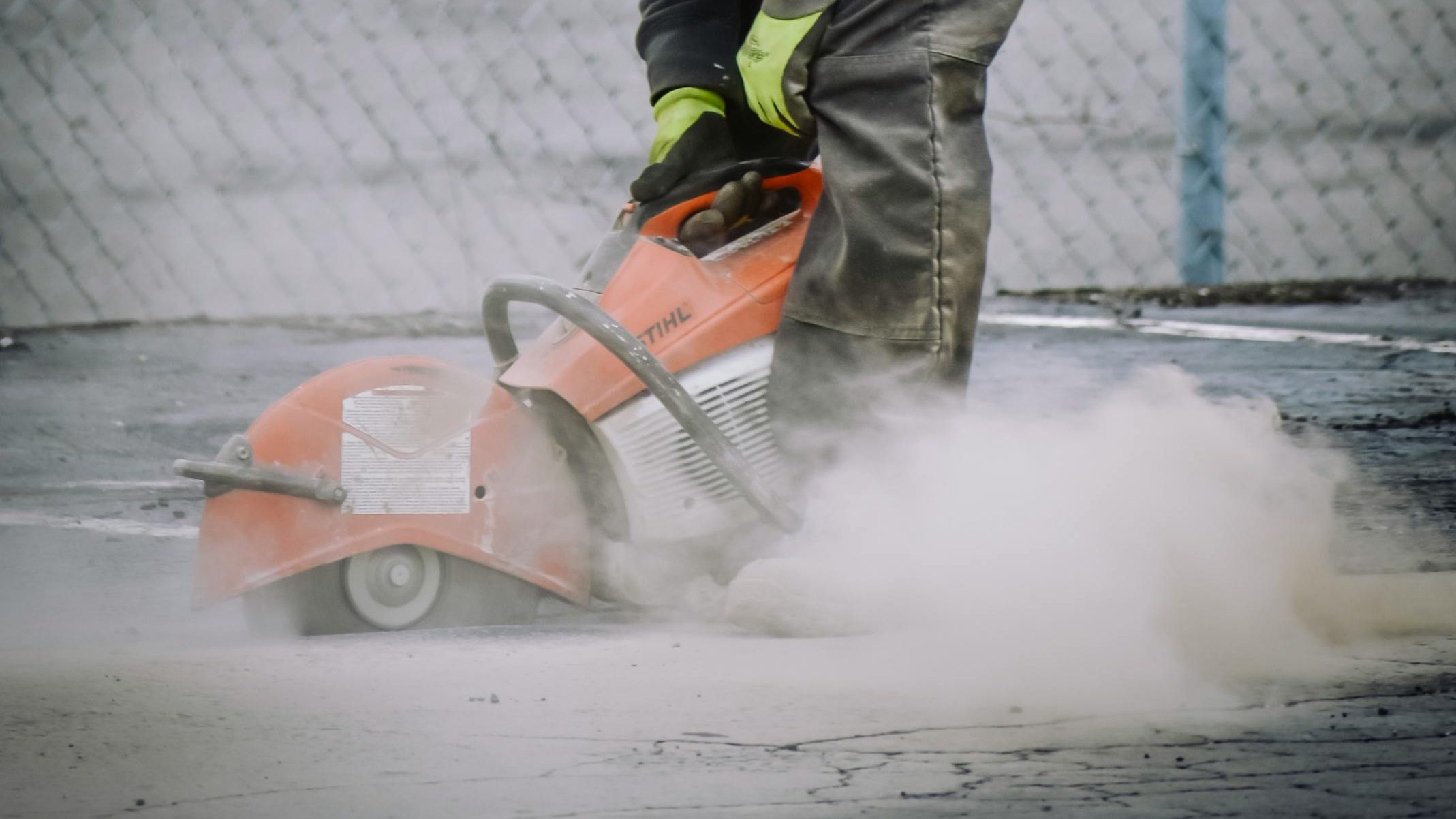 Worker with protective gear cutting concrete with a saw in an outdoor setting.